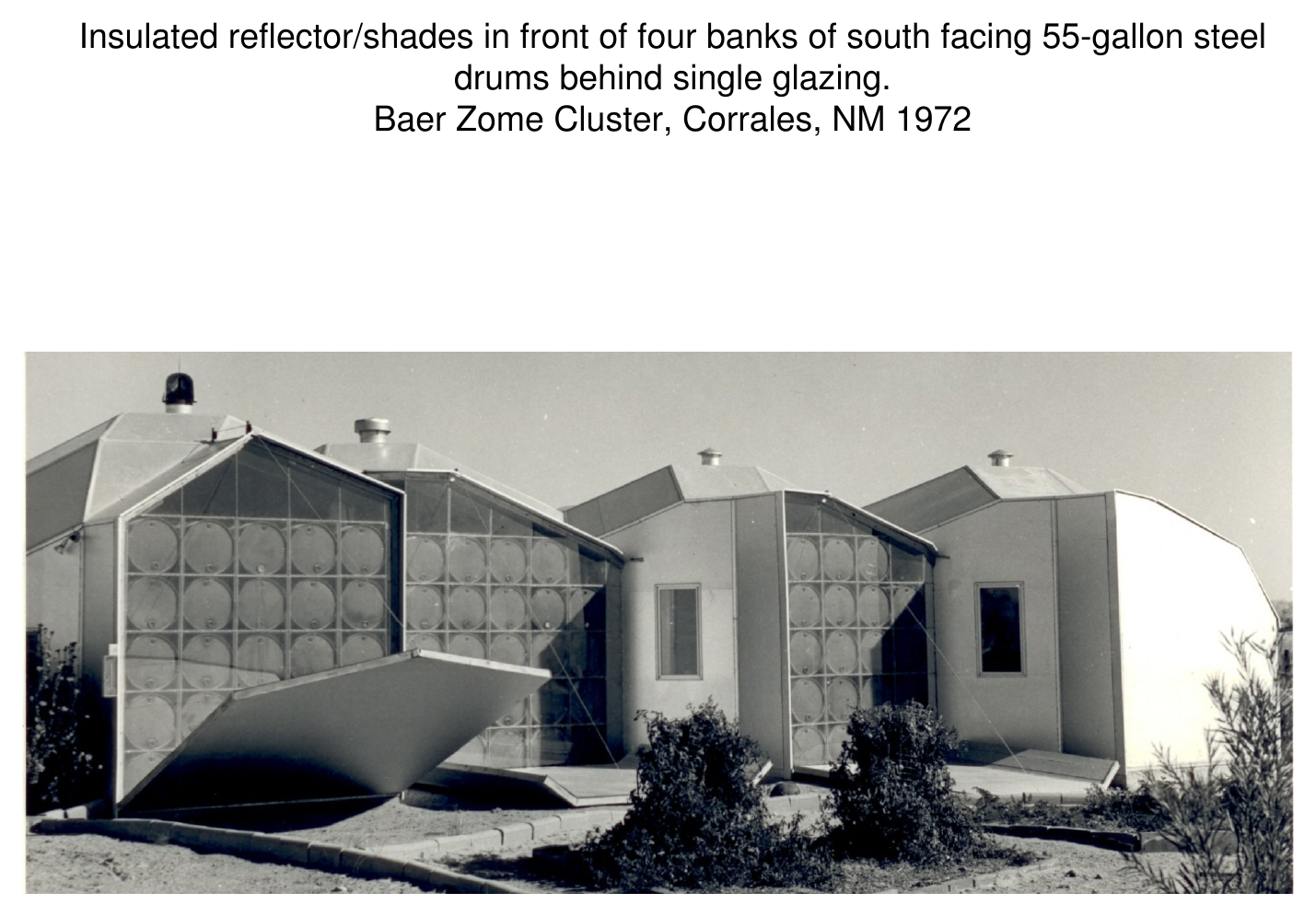 Photograph of angular Baer Zome Cluster houses with insulated reflector/shades in front of four banks of south-facing 55-gallon steel drums behind single glazing, Corrales, NM, 1972