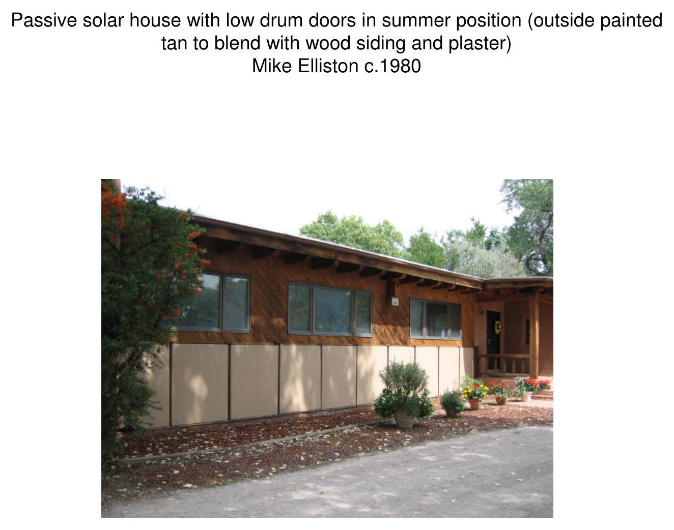 Exterior photograph of Mike Elliston's passive solar house with low drum doors in summer position, painted tan to blend with wood siding and plaster, c.1980