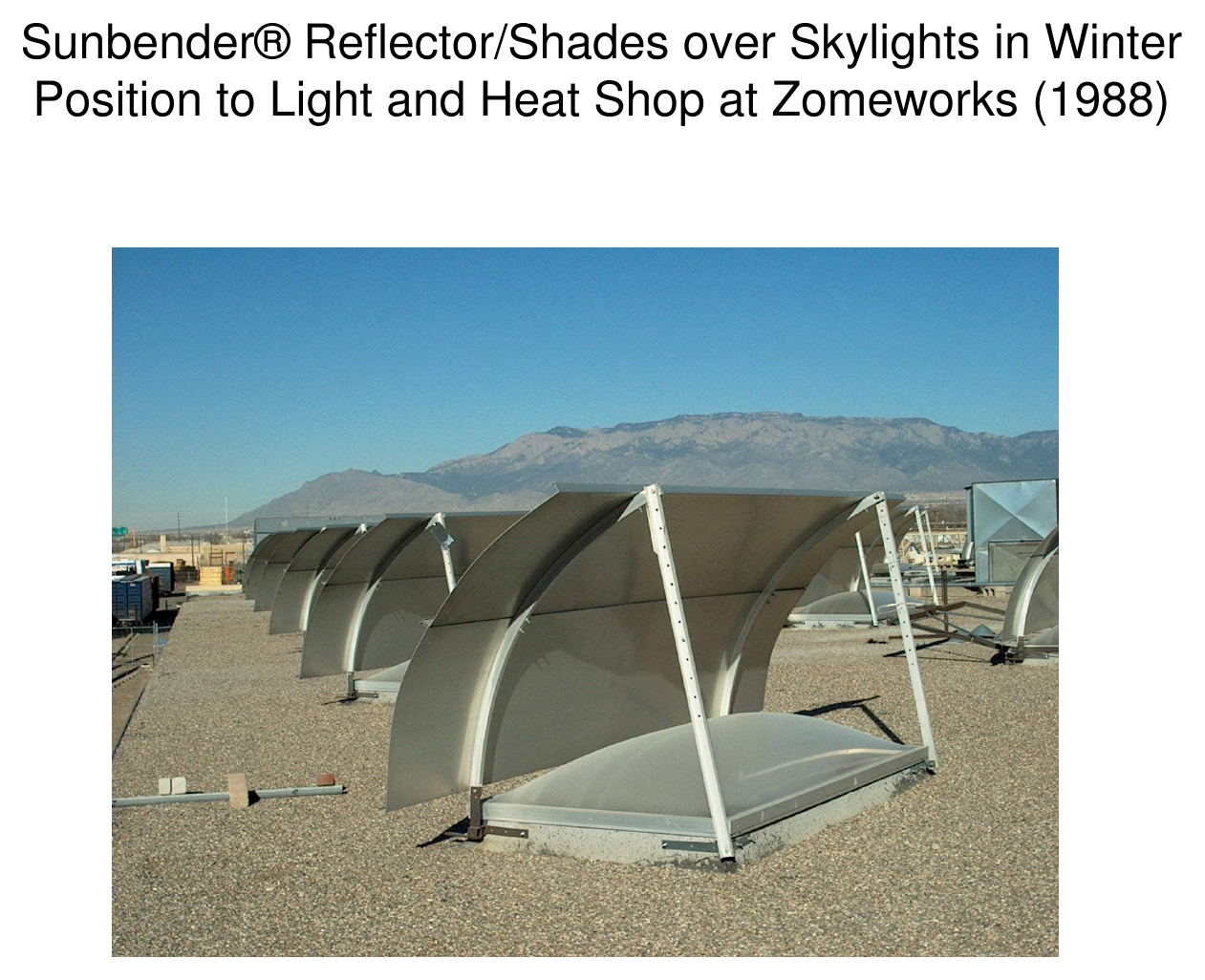 Rooftop photograph of Sunbender reflector/shades over skylights in winter position with the Sandia Mountains in the background, Zomeworks, 1988